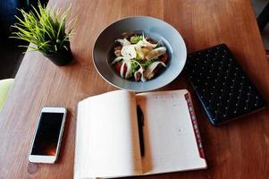 tisch mit telefon notizbuch, tablet und teller mit salat. foto