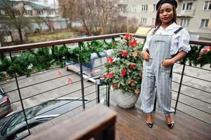 Afroamerikanerin in Overalls und Baskenmütze posierte auf der Außenterrasse mit Weihnachtsschmuck und Neujahrsbaum. foto