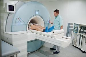 Der männliche Arzt schaltet das Magnetresonanztomographiegerät mit dem Patienten im Inneren ein. foto