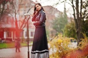 hübsches indisches mädchen in schwarzem saree-kleid und lederjacke posierte im freien auf der herbststraße. foto