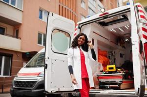 Afroamerikanische Sanitäterin, die vor einem Krankenwagen steht. foto