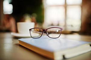 Nahaufnahme Foto von Notebook mit Brille gegen Tasse Kaffee am Café-Tisch. Brillenkonzept.