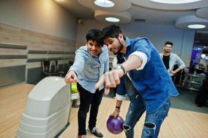 Südasiatischer Mann im Jeanshemd, der mit Ball an den Händen an der Bowlingbahn steht und zielt. Kerl bereitet sich auf einen Wurf vor. foto