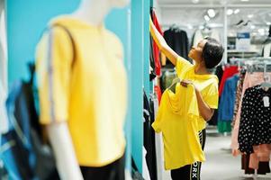 afroamerikanische Frauen in Trainingsanzügen, die im Sportswear-Einkaufszentrum gegen Regale einkaufen. sie wählt gelbes t-shirt. Sportgeschäft Thema. foto