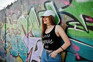 stilvolles, lässiges Hipster-Mädchen in Mütze und Jeans gegen große Graffiti-Wand.