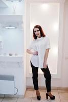 Brünettes wunderschönes Mädchen in der Boutique des Bekleidungsgeschäfts in Freizeitkleidung, weißer Bluse und schwarzer Hose. foto