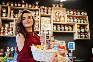 Mädchen in Rot, das verschiedene Produkte auf Korb im Feinkostgeschäft hält. foto