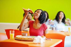 afrikanische frau mit pizza, die im restaurant gegen dunkelhäutige mädchen sitzt. foto