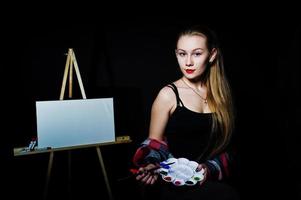 schöne Künstlerin Malerin mit Pinsel und Ölleinwand posiert im Studio isoliert auf schwarz. foto