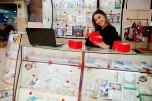 Porträt einer jungen kaukasischen Verkäuferin mit roten Geschenkboxen. kleines Geschäft mit Süßigkeiten-Souvenir-Shop. foto