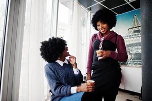 zwei lockige haare afroamerikanerin tragen pullover mit tassen tee, die im café drinnen gestellt werden. foto