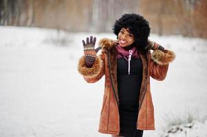 lockiges haar afroamerikanerin trägt schaffellmantel und handschuhe, die am wintertag gestellt werden, zeigen fünf finger. foto