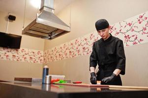 professionelle kochkleidung in schwarz, die sushi und brötchen in einer restaurantküche mit japanischer traditioneller küche herstellt.