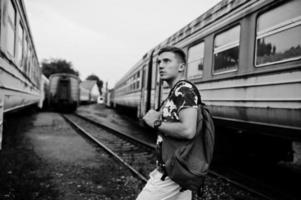 Lifestyle-Porträt eines gutaussehenden Mannes mit Rucksack, der auf dem Bahnhof posiert. foto