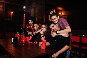 gruppe indischer freunde, die spaß haben und sich im nachtclub ausruhen, cocktails trinken und shisha rauchen. foto