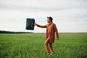 Stilvoller Mann mit Brille, brauner Jacke und Hut mit Tasche auf der grünen Wiese. foto