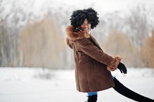 lockiges haar afroamerikanerin trägt schaffellmantel und handschuhe, die am wintertag gestellt werden. foto