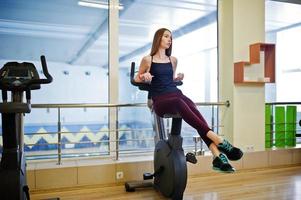 junge sportmädchen trainieren im fitnessstudio. fitnessfrau, die übungen auf stationärem fahrrad macht. foto