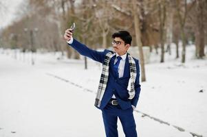 stilvoller indischer studentenmann in anzug, brille und schal posierte am wintertag im freien und machte selfie. foto