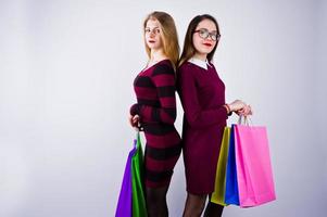 Zwei schöne Freundinnen in Kirschkleidern posieren mit bunten Einkaufstüten im Studio. foto
