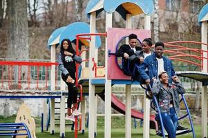 junge tausendjährige afrikanische freunde auf spielplatz, rutsche und schaukel. glückliche schwarze leute, die zusammen spaß haben. generation z freundschaftskonzept. foto