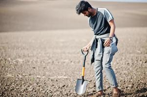 Südasiatischer agronomischer Bauer mit Schaufel, der schwarzen Boden inspiziert. landwirtschaftliches Produktionskonzept. foto