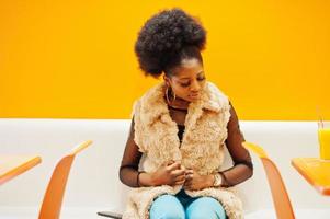 afrikanische frau mit afrohaar, die auf café gegen orange wand sitzt. foto