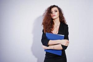 brünettes lockiges Mädchen in schwarzer Bürojacke mit Rock, auf BH mit Ordner mit Dokumenten in Händen auf Studio vor weißem Hintergrund. sexy Geschäftsfrau. foto