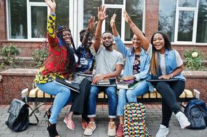 Gruppe von fünf afrikanischen College-Studenten, die gemeinsam Zeit auf dem Campus des Universitätshofs verbringen. schwarze afrofreunde, die an der bank mit schulsachen, laptops notizbüchern studieren. foto