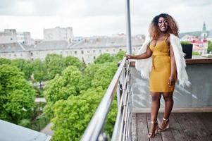 glamouröse afrikanisch-amerikanische frau im gelben kleid und im weißen wollumhang posierte auf dem balkon. foto