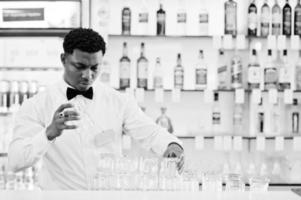 afroamerikanischer barkeeper trägt an der bar eine fliege, die eine brille putzt. foto