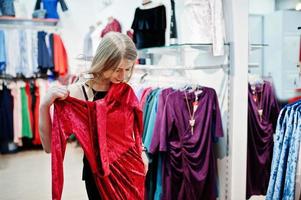 Blondes Mädchen probiert ein rotes Kleid in der Boutique an. foto