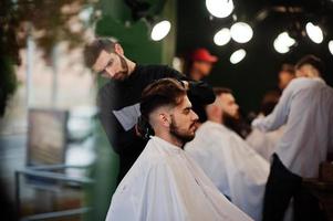 hübscher bärtiger mann im friseursalon, friseur bei der arbeit. foto