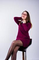 Porträt einer jungen Frau in lila Kleid und Brille, die auf dem Stuhl im Studio sitzt. foto