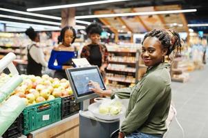 Gruppe afrikanischer Frauen wiegt Äpfel in Polyethylenbeuteln im Supermarkt. foto