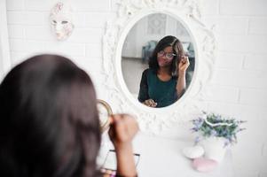 hübsche afroamerikanische frau mit make-up-palette in den händen, die spiegel betrachten. foto