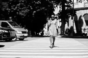 stilvolle afroamerikanische frau, die auf zebrastreifen oder fußgängerüberweg geht und mit dem handy spricht. foto