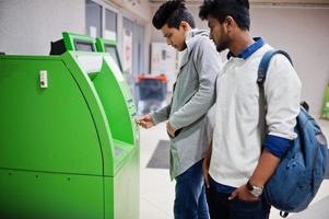 Zwei Asiaten entnehmen Bargeld aus einem grünen Geldautomaten. foto