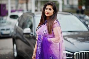 Indisches hinduistisches Mädchen im traditionellen violetten Saree posierte auf der Straße gegen schwarzes Business-SUV-Auto. foto