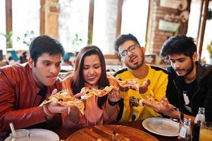 gruppe asiatischer freunde, die pizza während der party in der pizzeria essen. glückliche indische leute, die zusammen spaß haben, italienisches essen essen und auf der couch sitzen. foto