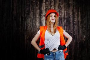 ingenieurin in orange schützt helm und gebäudejacke vor holzhintergrund. foto