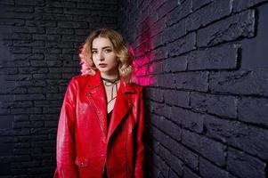 Studioporträt eines blonden Mädchens in roter Lederjacke gegen eine Ziegelwand. foto