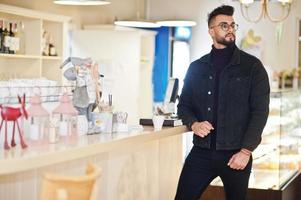 arabischer mann trägt schwarze jeansjacke und brille im café und trinkt kaffee an der bar. stilvoller und modischer arabischer Modelltyp. foto