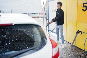 südasiatischer mann oder indischer mann, der seinen weißen transport auf autowaschanlage wäscht. foto