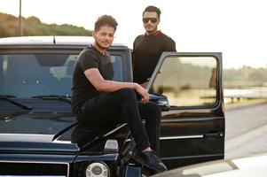 zwei asiatische brüder tragen alles in schwarz und posieren in der nähe eines suv-autos. foto