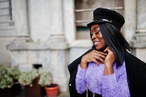 Afroamerikanerin in violettem Kleid und Mütze posierte im Freien. foto