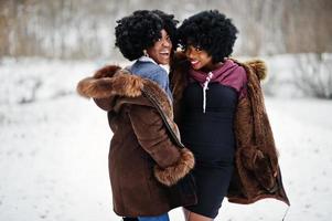 zwei lockige haare afroamerikanerinnen tragen einen schaffellmantel und handschuhe, die am wintertag gestellt wurden. foto