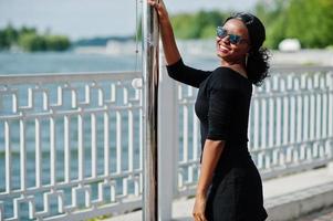 Afroamerikanisches Mädchen mit Sonnenbrille, schwarzer Kleidung und Hemd posierte im Freien. modische schwarze Frau. foto