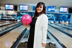 stilvolle asiatische frau, die an der bowlingbahn mit ball zur hand steht. foto