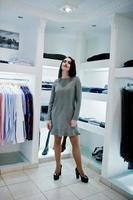 Brünettes wunderschönes Mädchen in der Boutique des Bekleidungsgeschäfts im grauen Kleid. foto